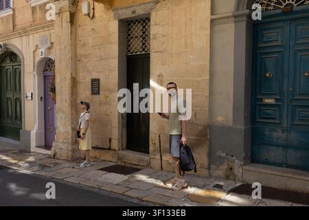 Valletta, Malta, June 19, 2026. Tourists stand on a sidewalk near historic building entrances. Stock Photo