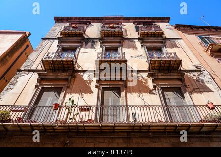 Low angle view of a historic weathered building facade with multiple ornate iron balconies and potted plants in Bosa, Sardinia, Italy Stock Photo
