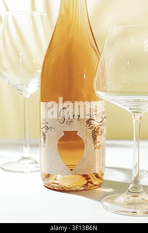 A bottle of Gura wine is placed on a table beside two empty wine glasses. Natural light shines through, highlighting the bottle and glasses Stock Photo
