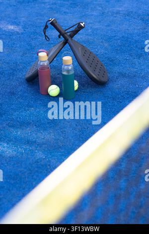 Black perforated paddles are crossing on blue court with red and teal bottles, balls near net Stock Photo