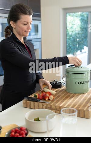 Woman wearing black zip-up jacket chopping strawberries on butcher-block cutting board near COMPOST Stock Photo
