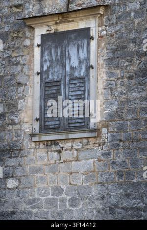 Close-up of a weathered stone wall with a gray shuttered window. Aged stonework and weathered shutters Stock Photo