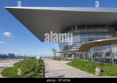 A view of the paved footpath along the quay, next to the green spaces of the Opera Park (Operaparken), with visitors sitting on a wooden bench in fron Stock Photo