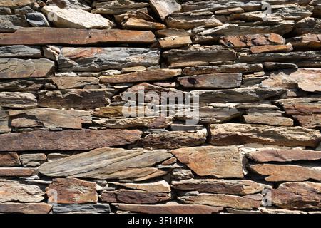 Close-up of a rustic dry stone wall with layered natural rocks creating a textured background Stock Photo