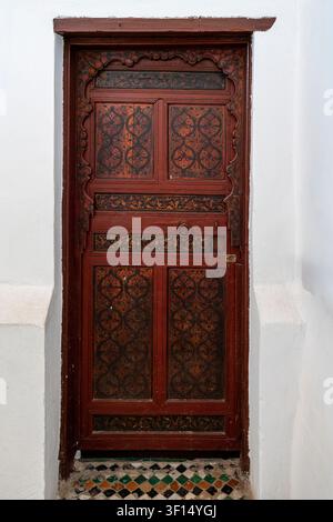 A tall single wooden door, displayed against a white wall as a museum exhibit, shows its rich carved wooden panels with arabesque floral patterns in d Stock Photo