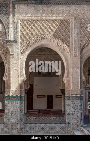 A close-up view of an arched opening in the Medersa Bou Inania shows the intricate transition from stucco arabesque carvings to the zellige tile bands Stock Photo