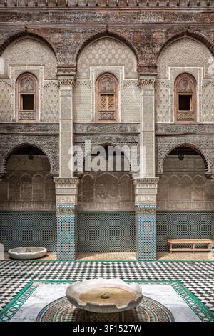 The interior courtyard of the Medersa Attarine shows the central marble fountain basin surrounded by a checkered black and white marble floor, the orn Stock Photo
