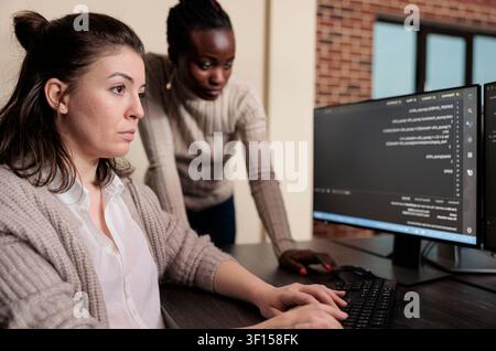 Multiracial tech engineers program an application on computers, encrypting cloud processing data through blockchain security workflows, linking developer team and cyber security. Stock Photo