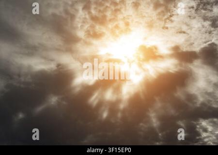 Dramatic background with warm sun rays penetrating dark clouds Stock Photo