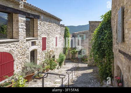 Picturesque natural stone exit with metal handrail, lined with planted stone houses with red shutters, to an artist's studio with bright green door at Stock Photo