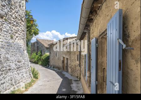 Narrow, asphalted alleyway in the historic town center with old stone houses, open light blue wooden shutters and a historic alleyway lamp under a blu Stock Photo