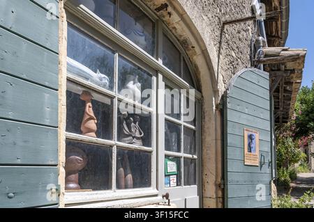 View of the shop window of an art studio and pottery studio with ceramic sculptures and clay figures on display behind lattice windows next to open, p Stock Photo