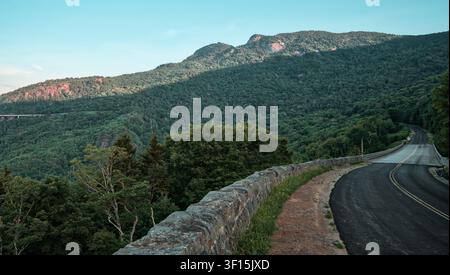 A paved mountain road curves past a stone wall and forested slopes on Grandfather Mountain in North Carolina. Stock Photo