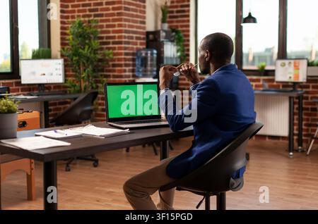 Businessman views a horizontal green screen on his laptop while planning a project, using a chroma key display and isolated mockup template in the office. Stock Photo