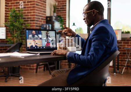Entrepreneur joins a video conference on a laptop to work with colleagues, plan strategy and discuss a project from an office desk. Stock Photo