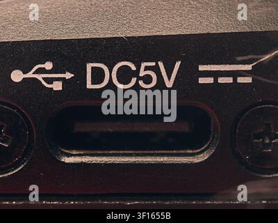 Macro closeup of a DC 5V USB charging power input slot on a textured black electronic device panel flaked by two phillips head screws Stock Photo