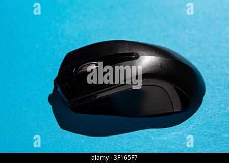 Studio shot of a black wireless computer mouse isolated on a bright blue background, representing computer accessories, office equipment, and modern t Stock Photo