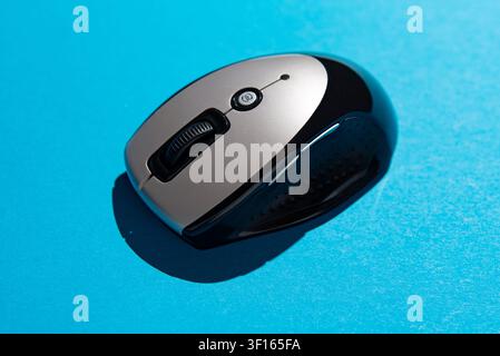 Studio shot of a black and silver wireless computer mouse isolated on a bright blue background, representing computer accessories, office equipment, a Stock Photo
