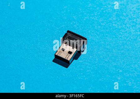 Studio shot of a small black USB wireless receiver dongle isolated on a bright blue background, representing computer accessories, connectivity, and m Stock Photo