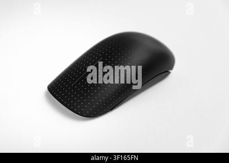 Studio close-up of a black wireless computer mouse with a dotted textured surface placed on a clean white background. Suitable for themes of computer Stock Photo