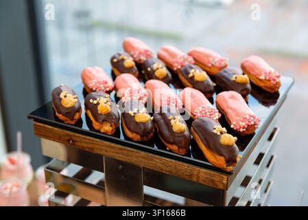 Delicious eclairs with pink glaze and chocolate topping decorated with nuts and sprinkles served on glass tray. Stock Photo