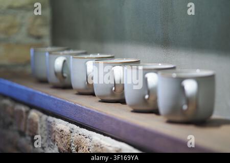 Ceramic mugs lined up on a rustic wooden shelf Stock Photo
