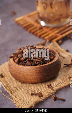 Rich cloves resting in a wooden bowl on a textured surface Stock Photo