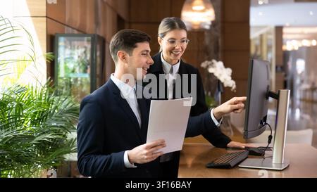 Two colleagues working on paperwork at hotel front desk Stock Photo