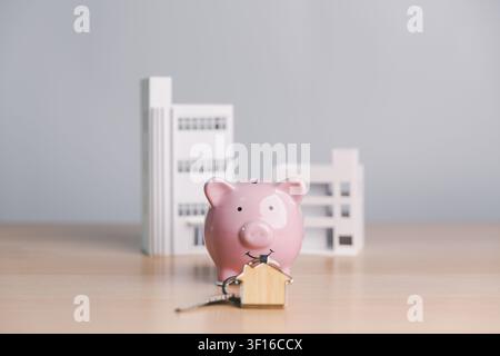Pink piggy bank with house key and modern building models, symbolizing property ownership, real estate savings, mortgage deposit, home buying, and inv Stock Photo
