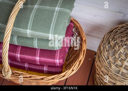 Folded wool blankets in wicker basket creating cozy rustic home interior storage Stock Photo