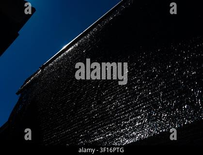 Low angle view of a black mesh shade cloth material canopy catching bright sunlight against a clear dark blue sky Stock Photo