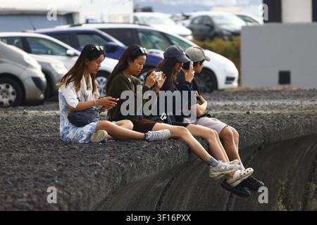 young travelers relaxing on a seaside promenade while using smartphones and taking photos during vacation in Tenerife. Stock Photo