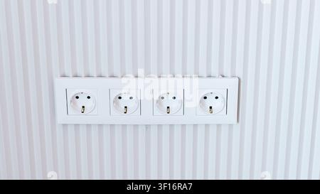 Four electrical power outlets are installed on a textured white wall with vertical stripes, offering multiple connection options for devices in a cont Stock Photo