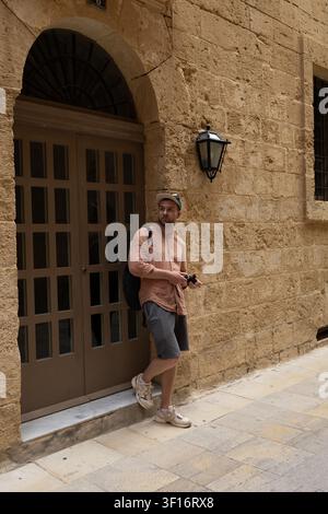 Young man with a camera standing near an ancient arched door on a historic stone street. Stock Photo