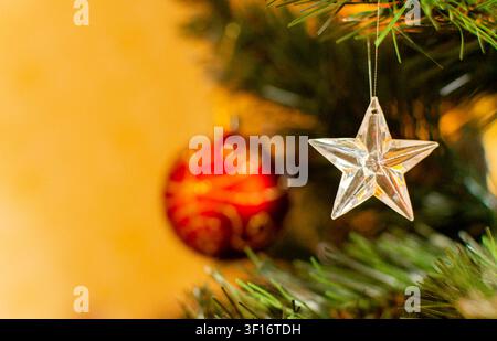 Silver star ornament hanging on a fir tree branch with blurred Christmas decoration. Holiday decoration for Christmas celebration, greeting cards and Stock Photo