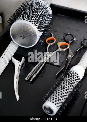 Professional hair stylist equipment including scissors, thinning shears, round brushes and a clip on a black work table Stock Photo