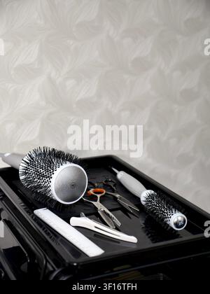 Professional hair stylist equipment including scissors, thinning shears, round brushes and a clip on a black work table Stock Photo
