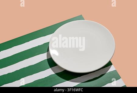 Minimalist food mockup with empty ceramic plate on striped green background. Flat lay concept for menu or recipe, High angle view of a blank round whi Stock Photo