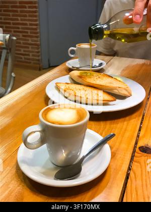 Cups of coffee and hand pouring olive oil on toast. Spain. Stock Photo