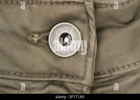 Closeup view of metal button on olive green denim pants. Textured fabric detail of casual trousers. Clothing element and manufacturing material qualit Stock Photo
