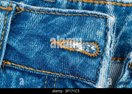 Close up view of blue denim jeans buttonhole with orange stitch. Educational macro detail of garment construction and textile texture. Fashion industr Stock Photo