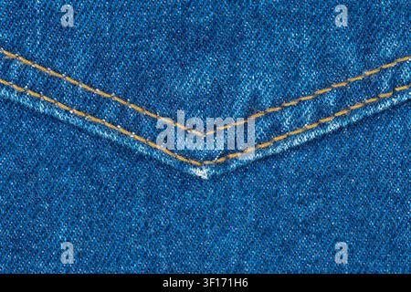 Macro photograph of classic blue denim material. Detailed view of jeans fabric texture shows V-shaped double seam with orange stitching. Ideal for fas Stock Photo