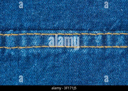 Closeup of blue denim fabric with orange stitching. Detailed texture of jeans material showing diagonal weave and sturdy seam. Textile background for Stock Photo