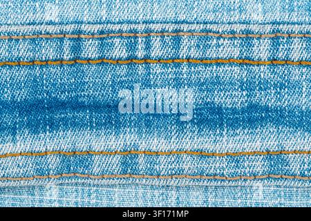 Macro view of blue jeans fabric. Detailed texture of classic denim with horizontal orange stitching. Background for fashion, clothing or textile desig Stock Photo