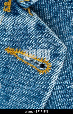 Closeup of buttonhole in blue denim fabric of jeans jacket. Macro texture of jeans cloth with yellow stitching. Fashion textile detail for garment man Stock Photo