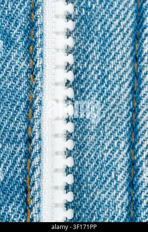 Extreme closeup of blue denim jeans material. Detailed macro shot shows fabric texture, orange stitching and white plastic zipper. Bright lighting hig Stock Photo