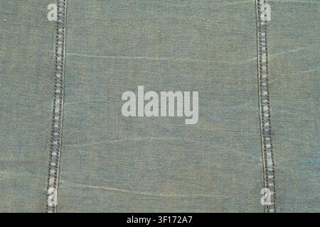 Textured denim fabric with visible double stitching in contrasting thread. Soft blue tones with natural wear patterns. Ideal for fashion, textile, bac Stock Photo