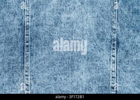 Detailed macro shot of light blue acid wash denim fabric. Classic textile background shows rough texture, diagonal weave, and two vertical seams. Retr Stock Photo