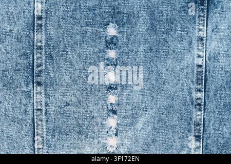 Light blue denim texture background. Distressed fabric with vertical rip, frayed white threads, and double seams. Casual, rugged clothing material for Stock Photo