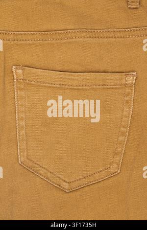 Macro detail of mustard yellow denim fabric. Back pocket of casual trousers shows texture, seams, and double stitching. Neutral background for fashion Stock Photo